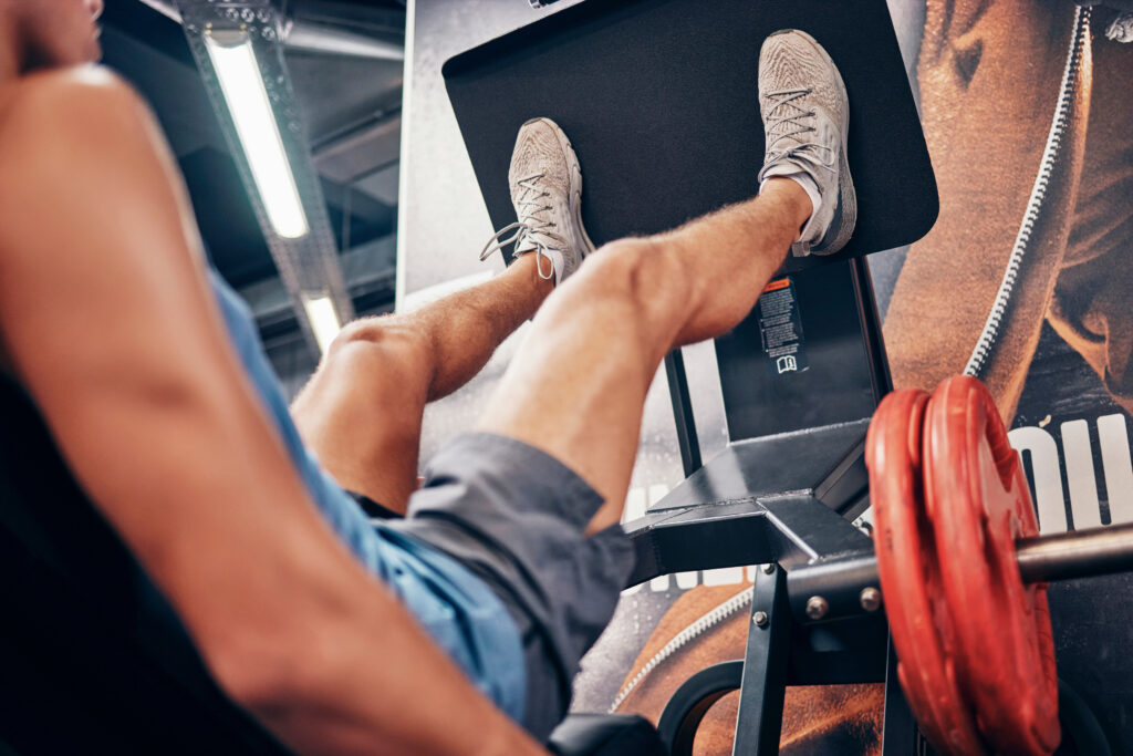 Homem realiza leg press em máquina durante treino de pernas na academia