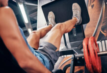 Homem realiza leg press em máquina durante treino de pernas na academia