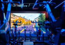 Sala de spinning da Cia Athletica com bicicletas ergométricas alinhadas, iluminação LED azul e painel de projeção imersivo ao fundo exibindo paisagem de estrada em canyon.