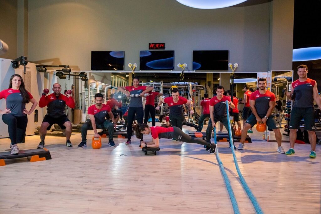 Como escolher uma academia com acompanhamento profissional de verdade? Instrutora corrige postura de aluna durante exercício com bola em academia.