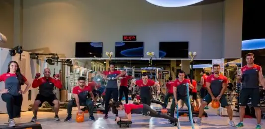Como escolher uma academia com acompanhamento profissional de verdade? Instrutora corrige postura de aluna durante exercício com bola em academia.