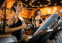 Mulheres correndo em esteiras em academia moderna com iluminação quente, durante treino cardiovascular focado em bem-estar e redução do estresse.