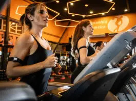 Exercício físico pode ajudar no estresse e na ansiedade? Mulheres correndo em esteiras em academia moderna com iluminação quente, durante treino cardiovascular focado em bem-estar e redução do estresse.