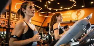 Mulheres correndo em esteiras em academia moderna com iluminação quente, durante treino cardiovascular focado em bem-estar e redução do estresse.