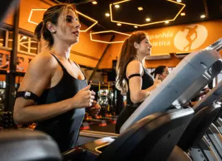 Mulheres correndo em esteiras em academia moderna com iluminação quente, durante treino cardiovascular focado em bem-estar e redução do estresse.