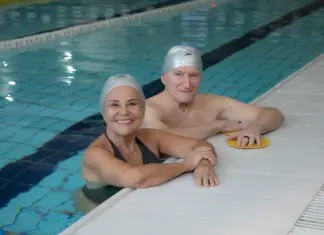 Programa Platinum da Cia Athletica: o segredo para envelhecer com mais saúde e autonomia Casal de idosos sorrindo dentro de uma piscina coberta da Cia Athletica, usando toucas de natação durante atividade do Programa Platinum
