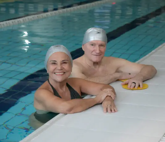 Programa Platinum da Cia Athletica: o segredo para envelhecer com mais saúde e autonomia Casal de idosos sorrindo dentro de uma piscina coberta da Cia Athletica, usando toucas de natação durante atividade do Programa Platinum