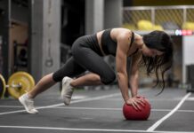 Mulher realiza exercício em posição de prancha com apoio sobre uma bola medicinal durante treino funcional de alta intensidade, representando o HIIT e o condicionamento cardiovascular.