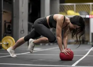 Mulher realiza exercício em posição de prancha com apoio sobre uma bola medicinal durante treino funcional de alta intensidade, representando o HIIT e o condicionamento cardiovascular.
