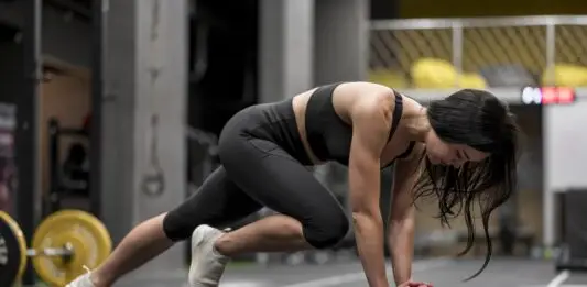 HIIT ou cardio contínuo: entenda as diferenças antes de escolher Mulher realiza exercício em posição de prancha com apoio sobre uma bola medicinal durante treino funcional de alta intensidade, representando o HIIT e o condicionamento cardiovascular.