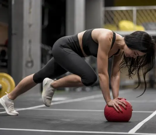 Mulher realiza exercício em posição de prancha com apoio sobre uma bola medicinal durante treino funcional de alta intensidade, representando o HIIT e o condicionamento cardiovascular.